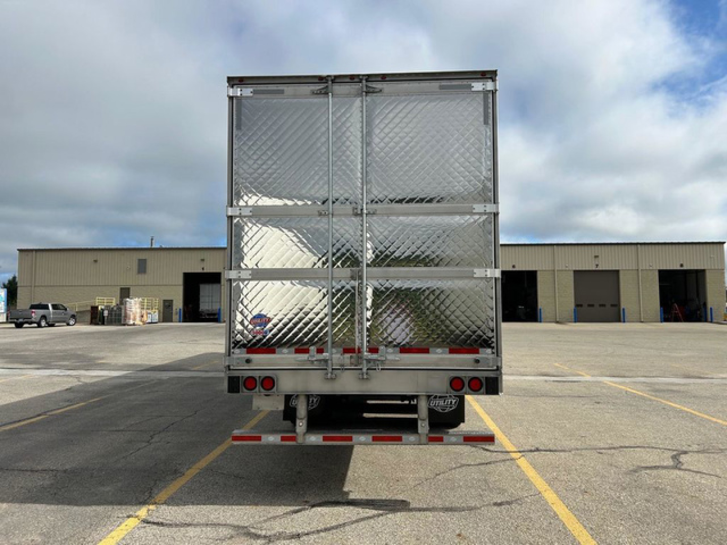 Trailer rear view of a new utility reefer trailer with diamond plate aluminum exterior and rear doors, in a dealership lot.