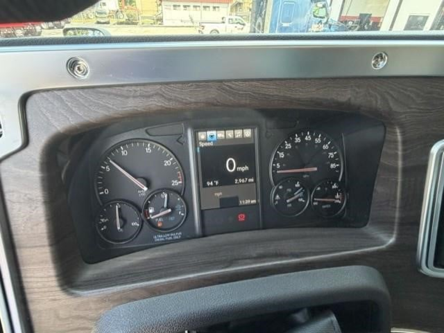 Truck instrument cluster showing speedometer, tachometer, and digital display; wood grain dash trim around gauges.