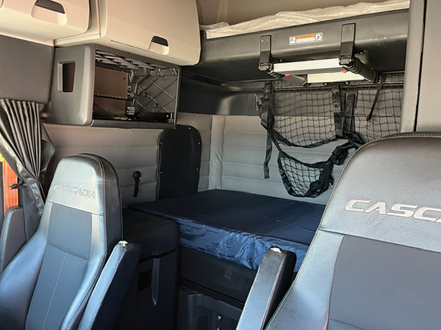 Truck cabin interior showing sleeper berth with storage nets and overhead cabinets in a Freightliner Cascadia126.