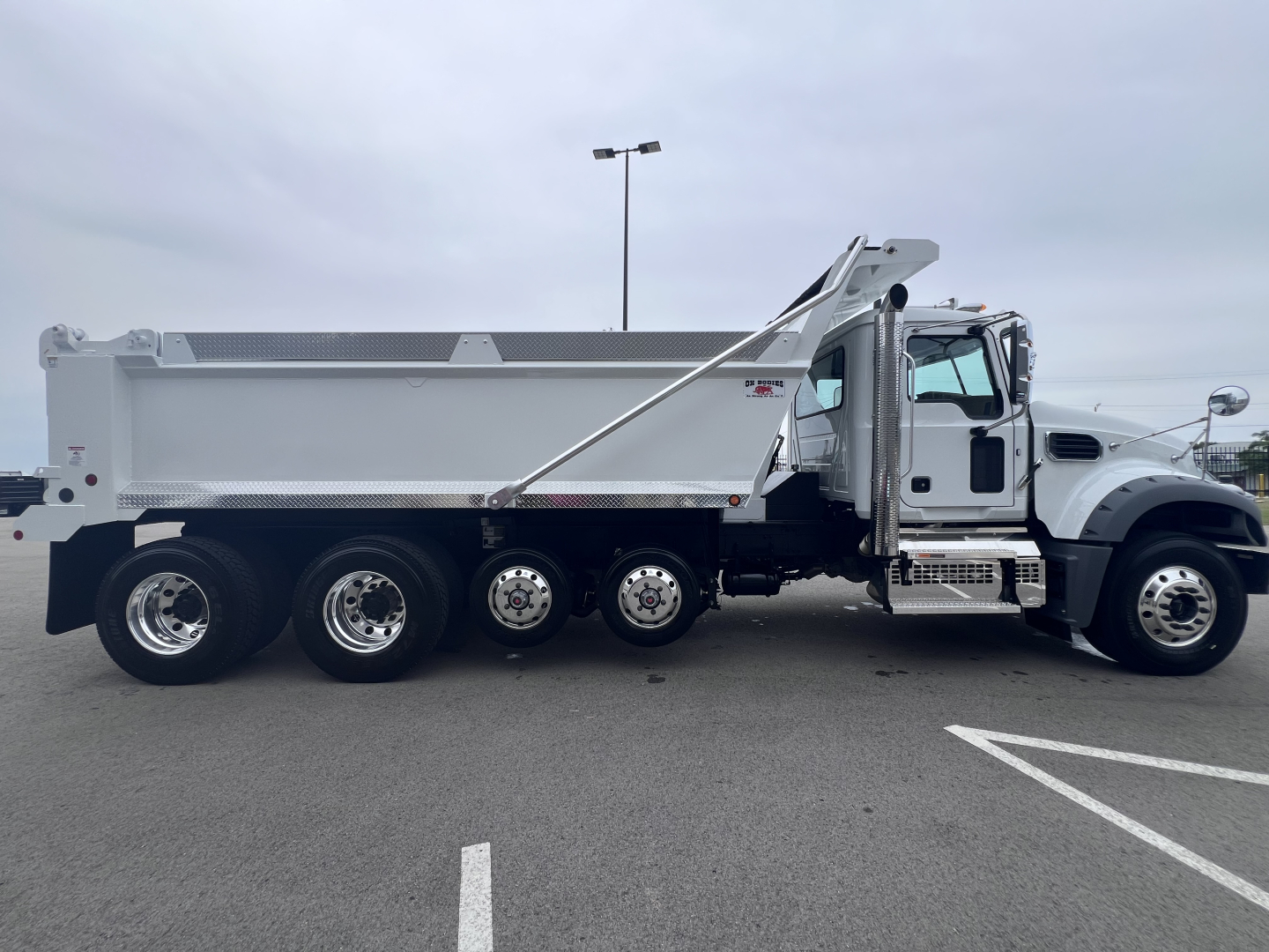 Dump truck side view showing Mack GR64F with dumping bed and chrome wheels.
