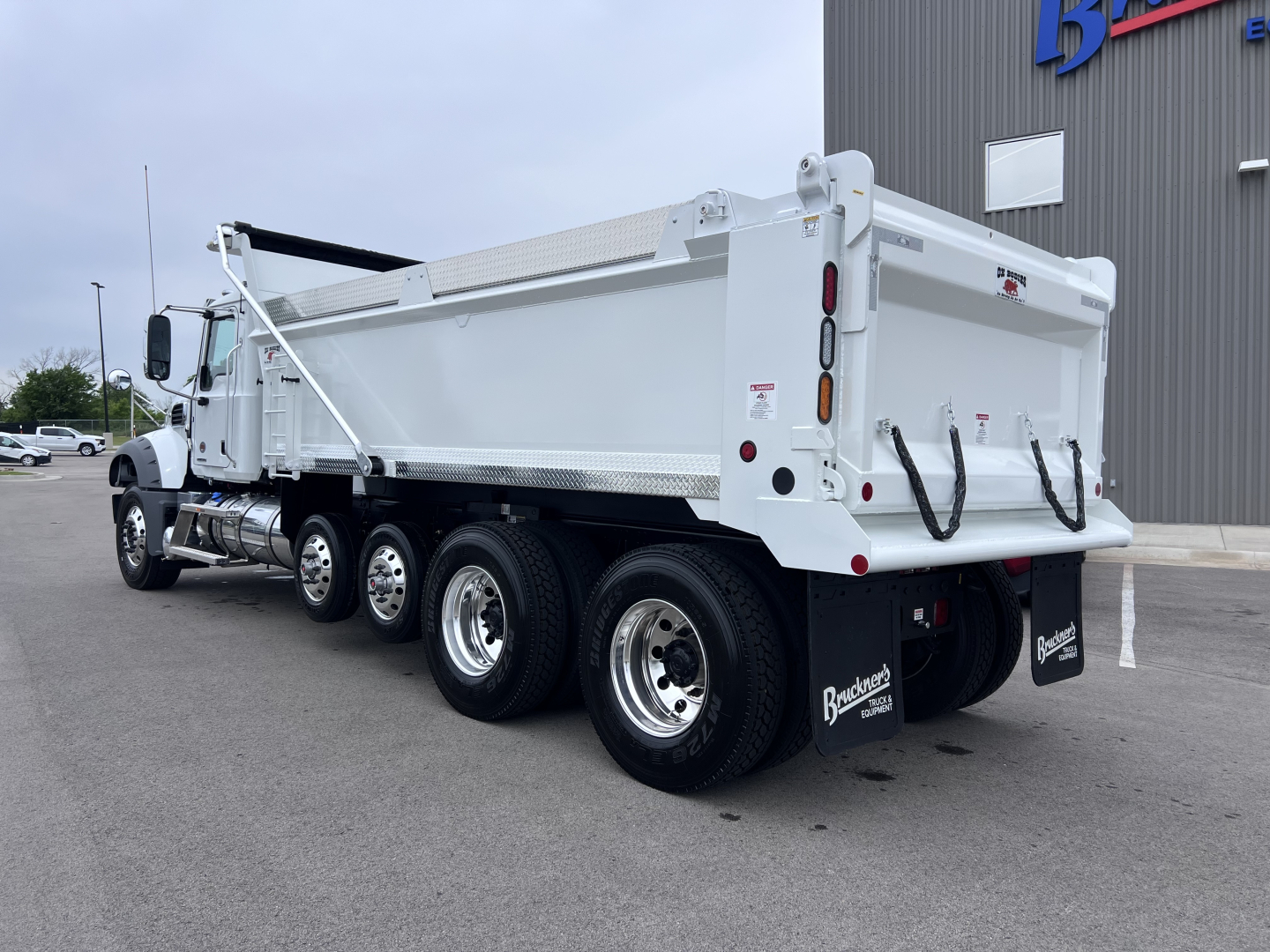 Dump truck rear three-quarter view showing dump bed and dual rear axles on a white Mack GR64F.