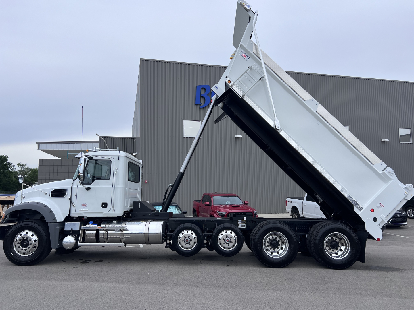 Mack GR64F dump truck in raised bed view showing cab and triple rear axles with towing hitch and hydraulic hydraulic hoses.