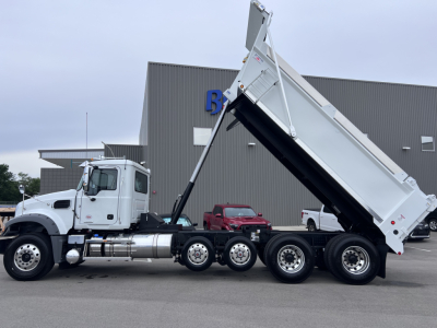 Mack GR64F dump truck in raised bed view showing cab and triple rear axles with towing hitch and hydraulic hydraulic hoses.