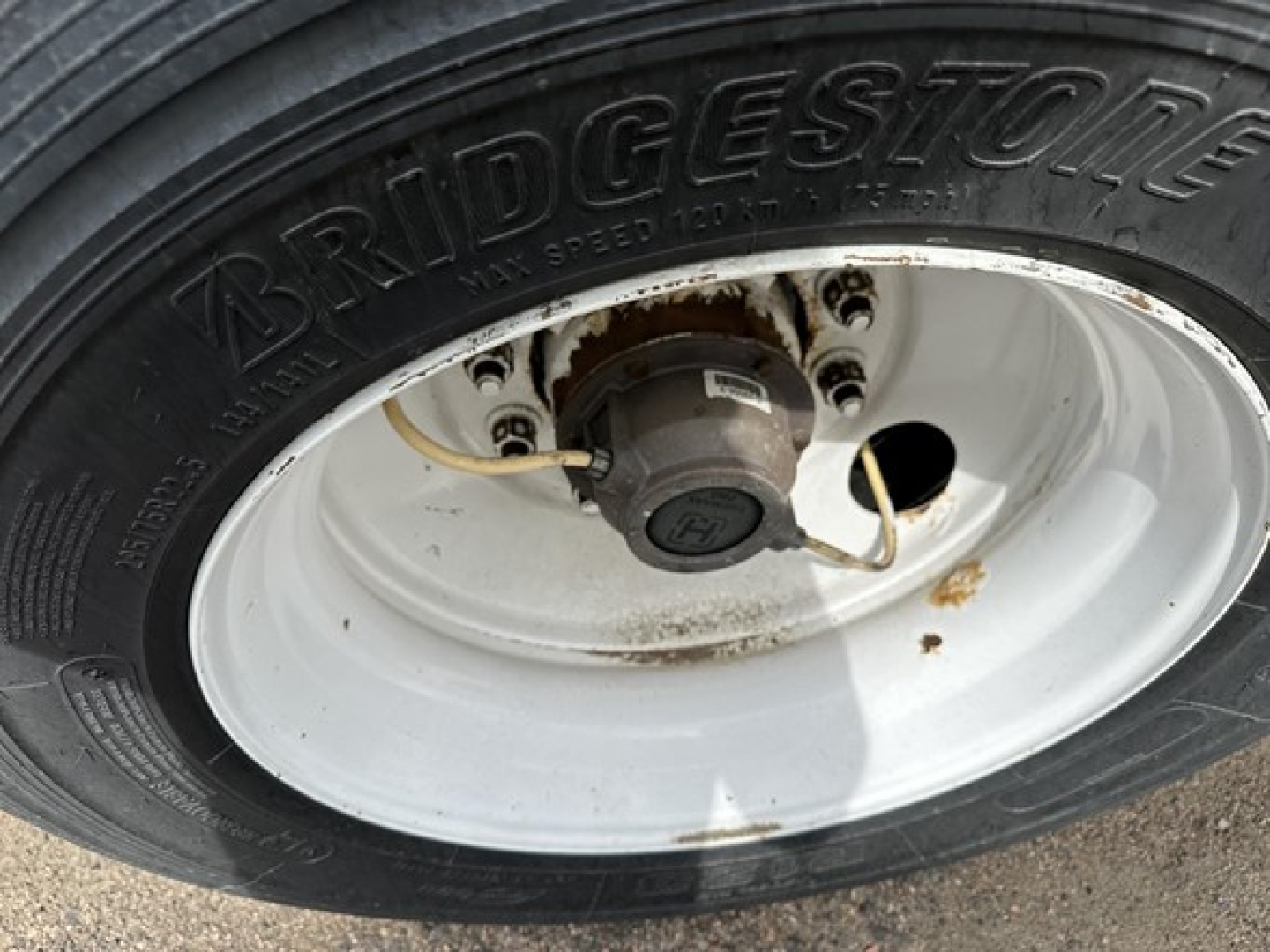 Bridgestone tire mounted on a white wheel with hub, showing brake drum and part of the axle; utility trailer context.