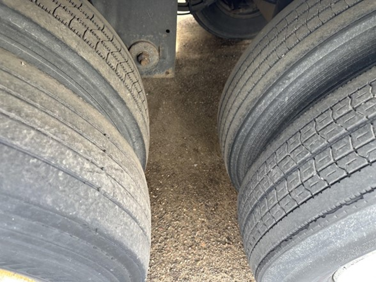 Dual rear trailer tires showing tread and gravel underneath; part of undercarriage and frame visible between wheels.