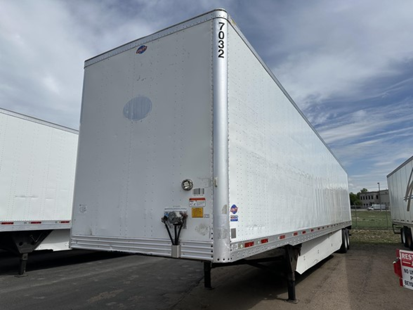 Trailer showing side and rear of a white Utility 4000D-X box trailer with unidentified stickers and VIN tag, front landing gear visible.