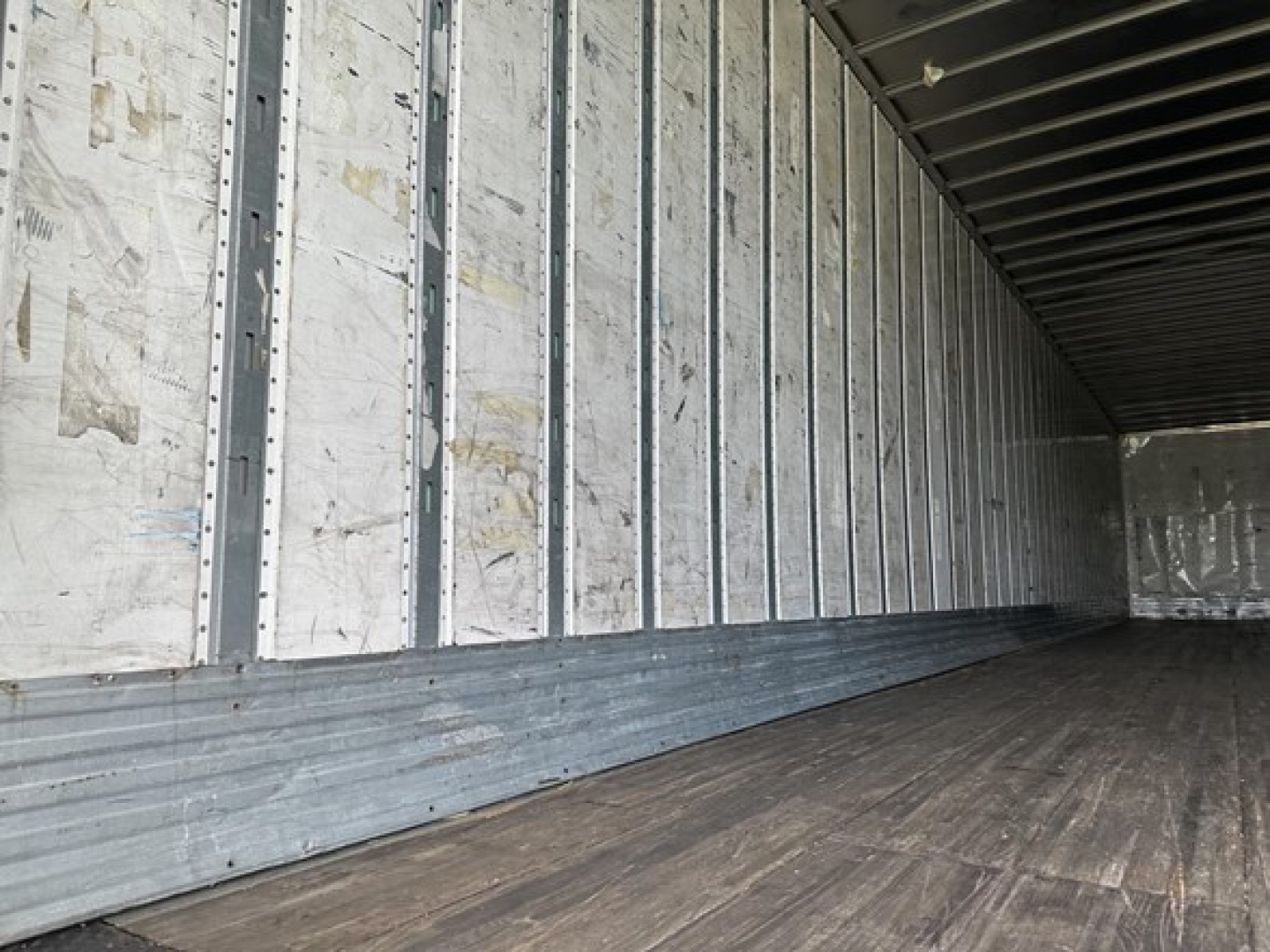 Trailer interior showing metal wall framing and wooden floor inside a box trailer.