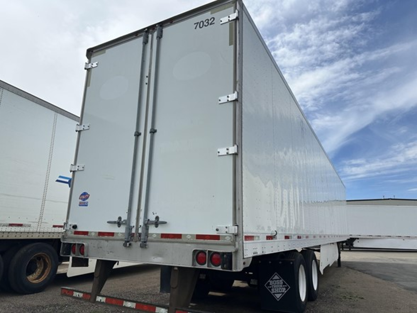 Rear view of a white utility trailer with double doors, stock number 7032 and the number 7032 on top door, taillights, and support legs visible.
