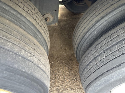 Dual rear trailer tires showing tread and gravel underneath; part of undercarriage and frame visible between wheels.