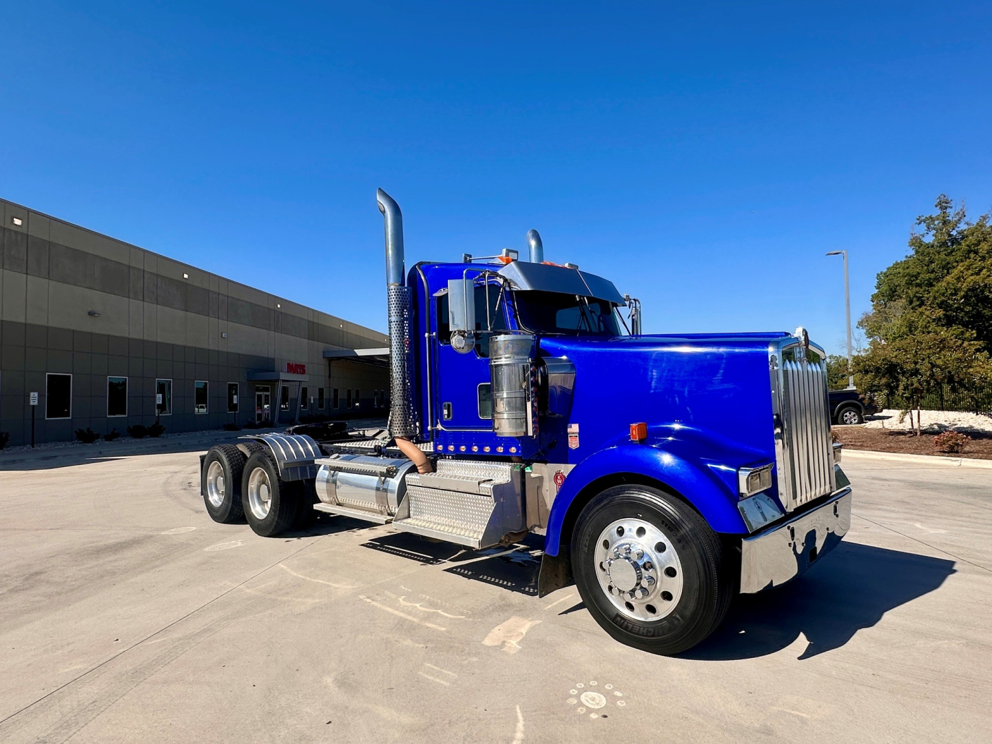 Kenworth W900 truck in blue showing side exhaust, chrome bumper, dual rear axles, and large grille.