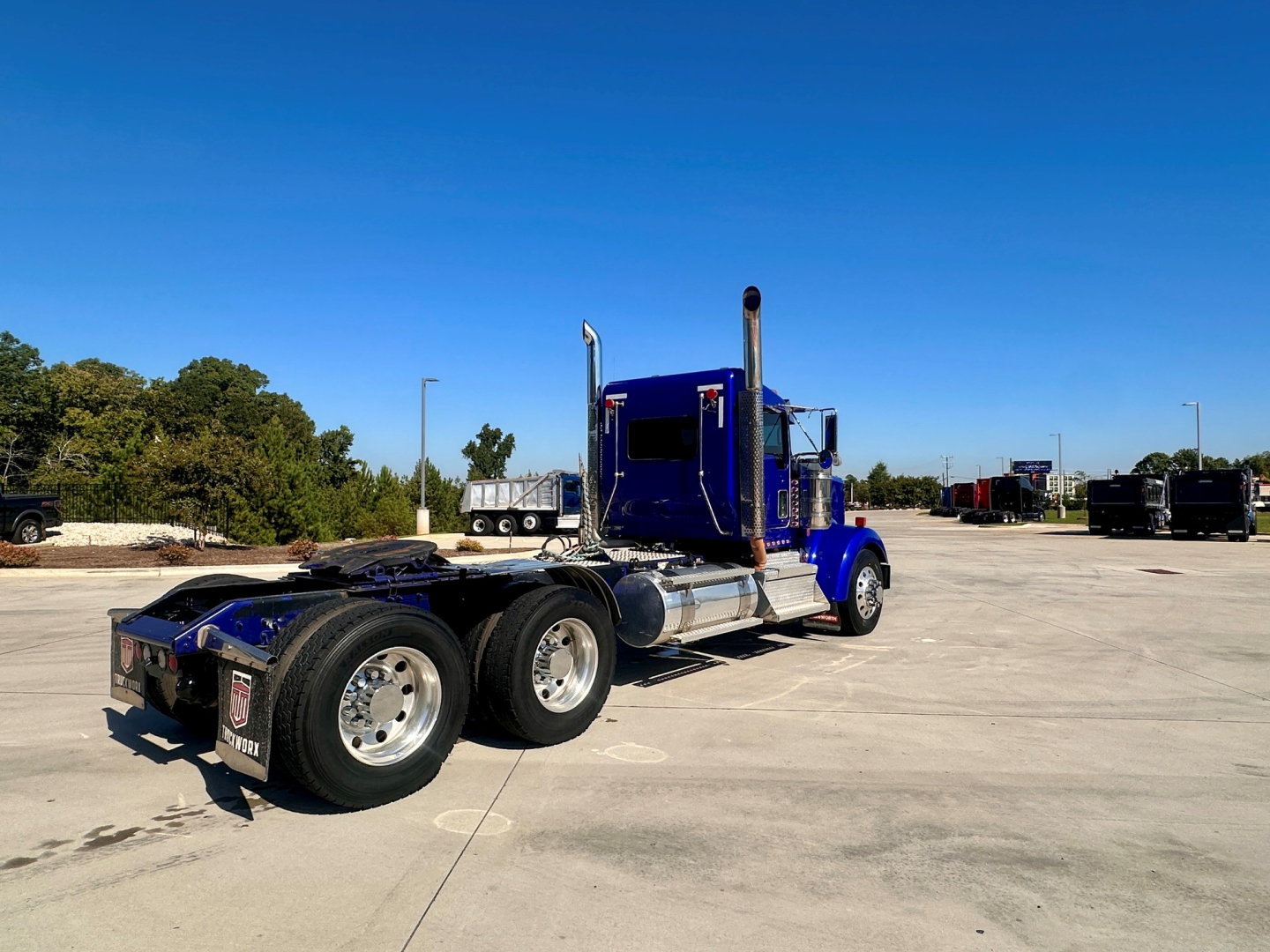 Kenworth W900 conventional daycab tractor in blue, side view showing rear dual rear axles, fuel tanks, and exhaust stacks.