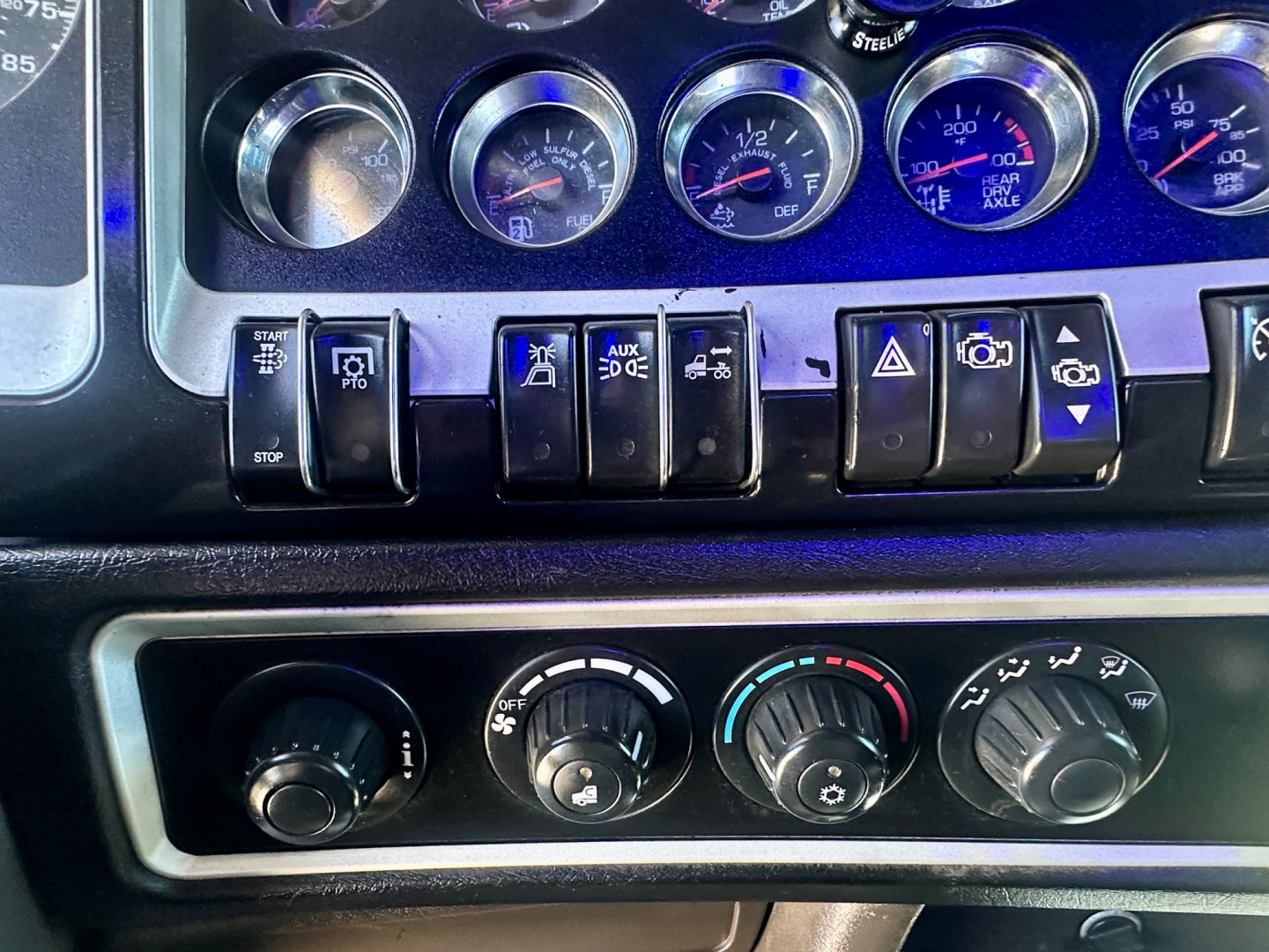 Dashboard panel of a 2021 Kenworth W900 showing multiple gauges and switches, with climate controls below.
