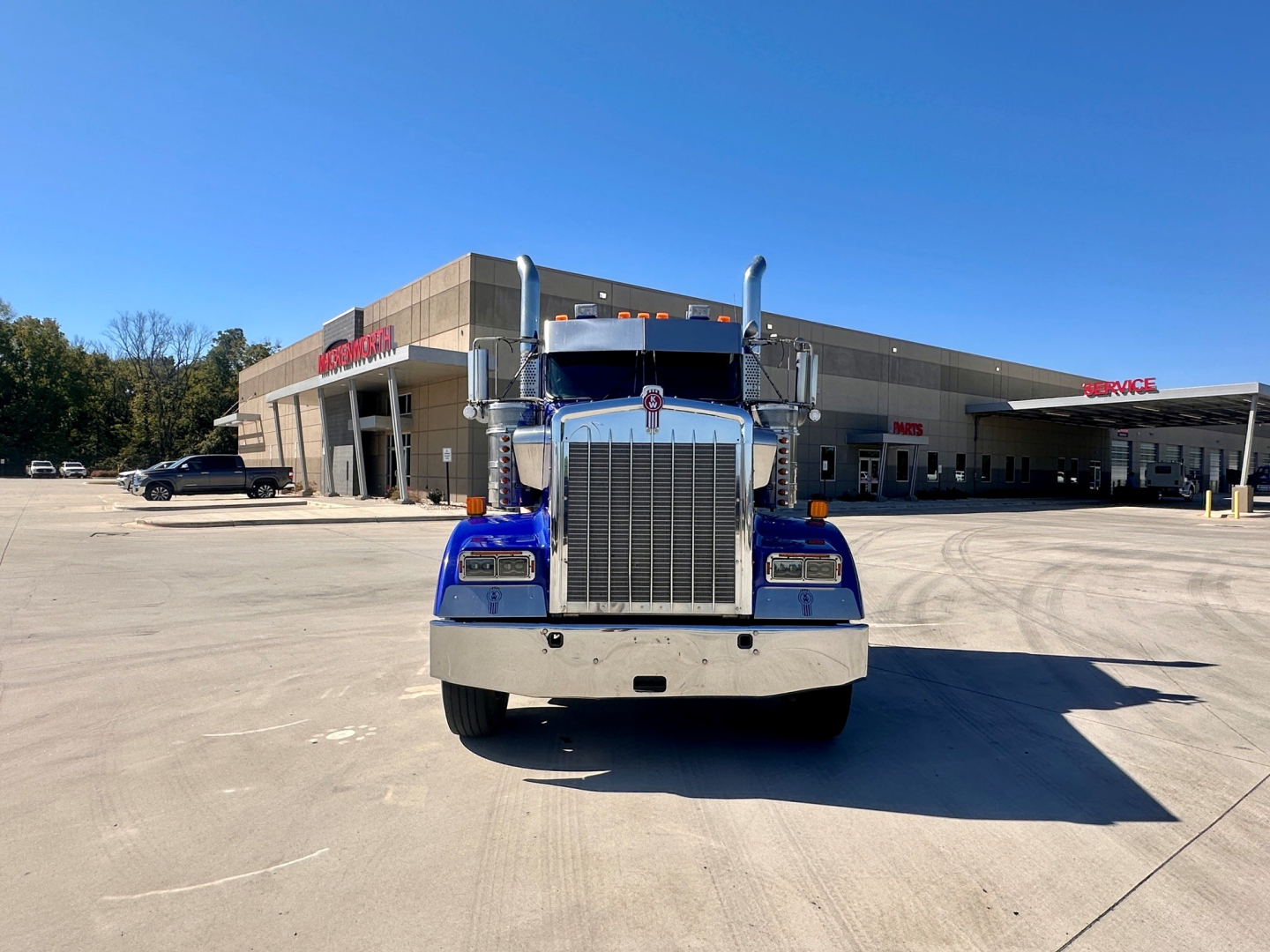 Kenworth W900 conventional daycab front view showing large chrome grille, blue cab, chrome bumper, tall exhaust stacks, and clear blue sky.
