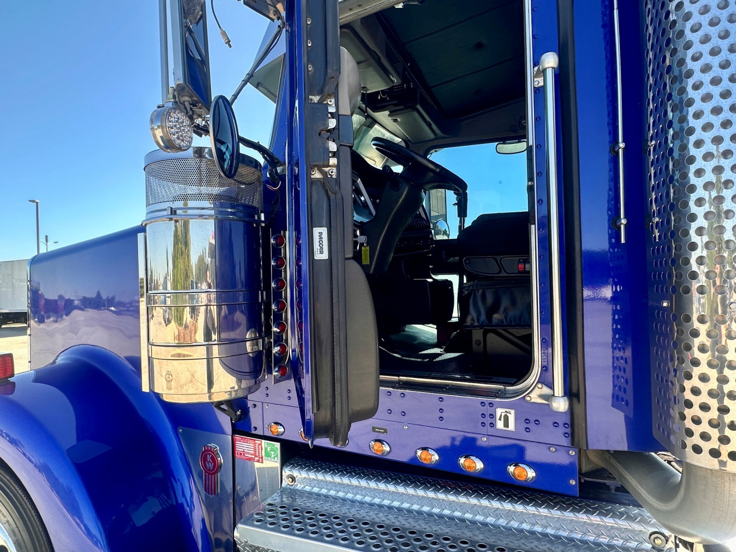 Kenworth W900 sleeper cab interior view through open door showing blue exterior and chrome fuel tank with diamond plate step.