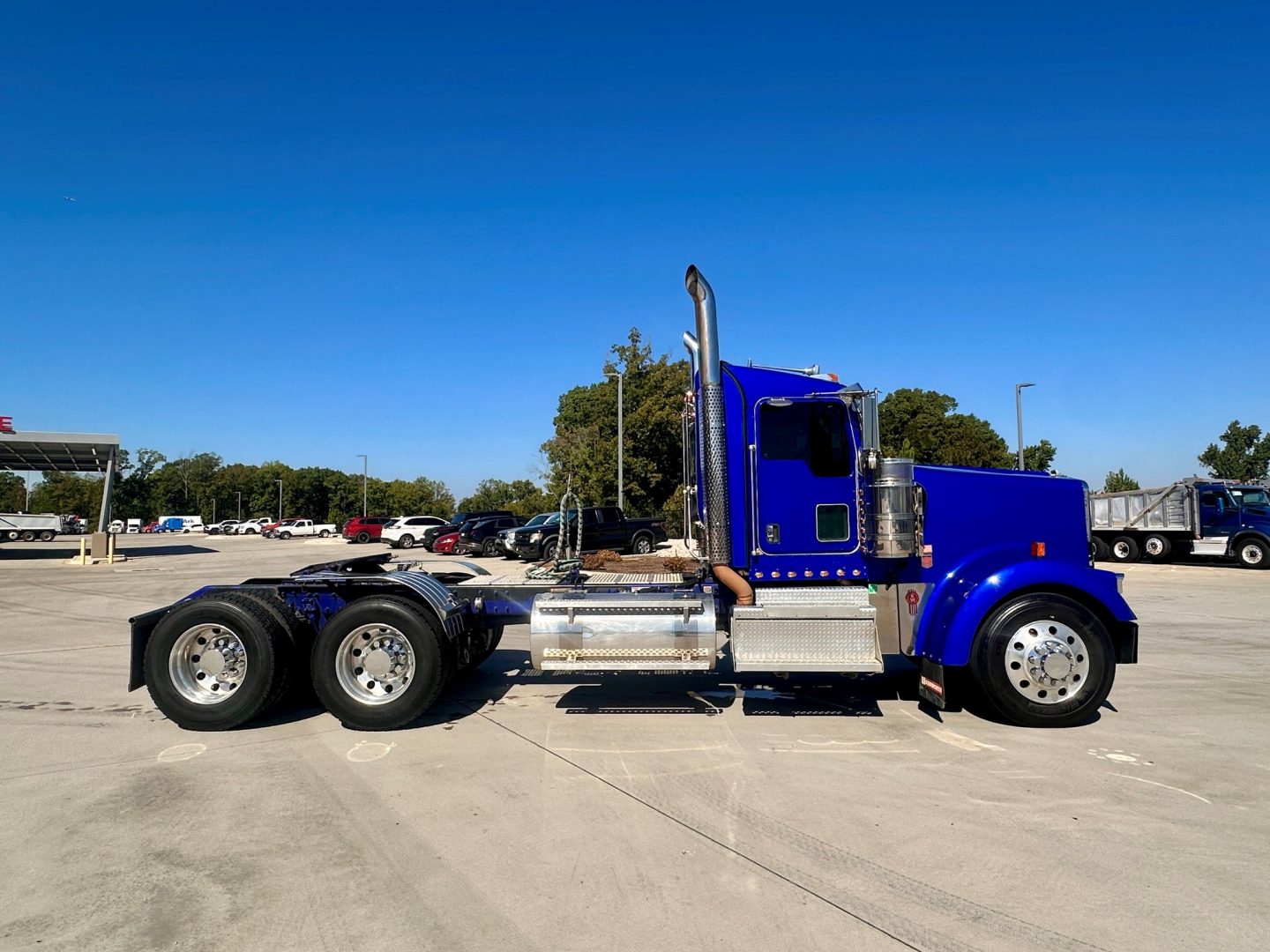 Kenworth W900 conventional daycab truck side view showing dual rear axles, blue exterior, chrome exhaust and fuel tanks, VIN 1XKWD49X6MR455849 visible on listing.