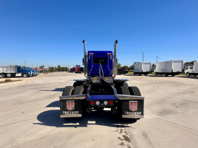 Rear view of a blue 2021 Kenworth W900 truck tractor showing dual rear axles and mud flaps with TruckWorx logos.