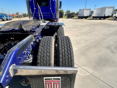 Kenworth W900 chassis and dual rear wheels in a truck yard, with blue glossy frame and metal steps visible.