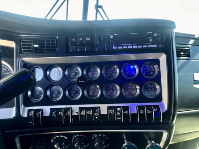 Kenworth W900 dash panel showing multiple gauges, switches, and an aftermarket radio unit.