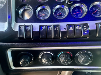 Dashboard panel of a 2021 Kenworth W900 showing multiple gauges and switches, with climate controls below.