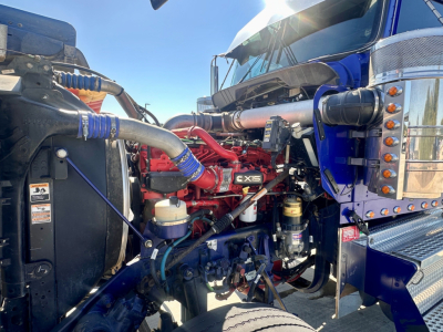 Kenworth W900 engine bay showing fuel lines, coolant reservoir, and red engine components labeled X15 proximity to blue cab.