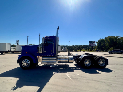 Kenworth W900 truck side profile with blue color, chrome tanks, and dual rear axles in a parking lot.