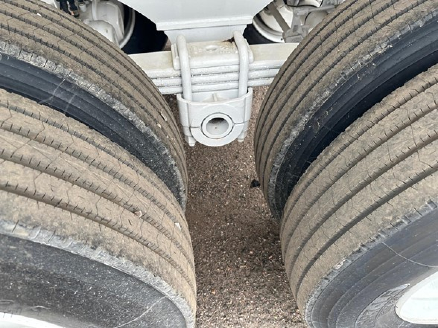 View of a dump trailer chassis showing tandem rear axles with dual tires and suspension components. Center hitch access hole visible between wheels.