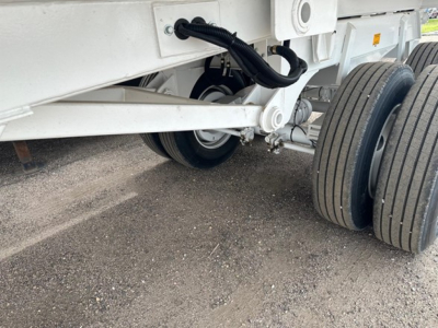 Trailer wheel hub view showing dual rear tires and undercarriage components of a dump trailer frame.
