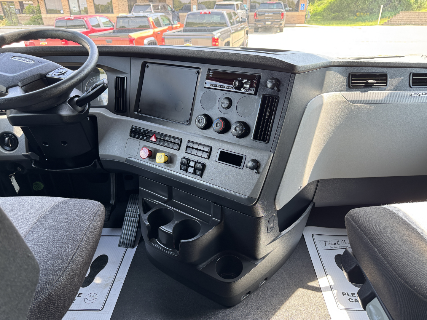 Cab interior of a Freightliner Cascadia 126 showing dashboard, steering wheel, and center console with gauges, controls, and cup holders.