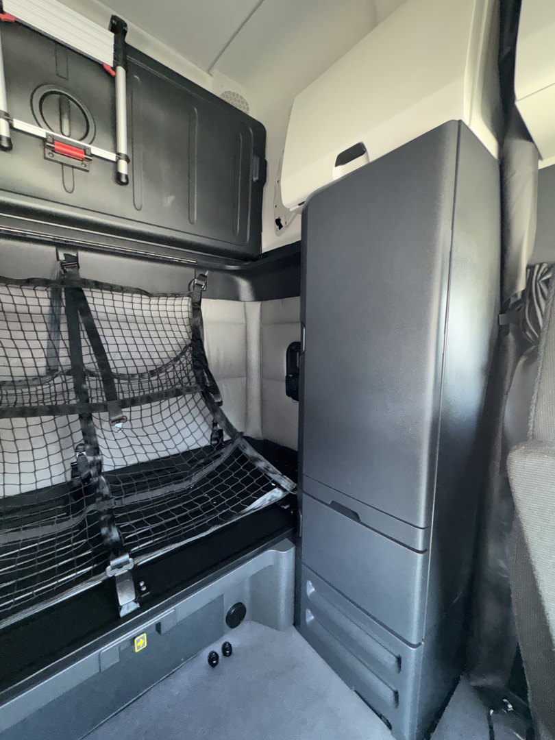 Freightliner Cascadia truck cabin interior showing storage compartments, a netted side compartment, and a vertical console with cabinets.