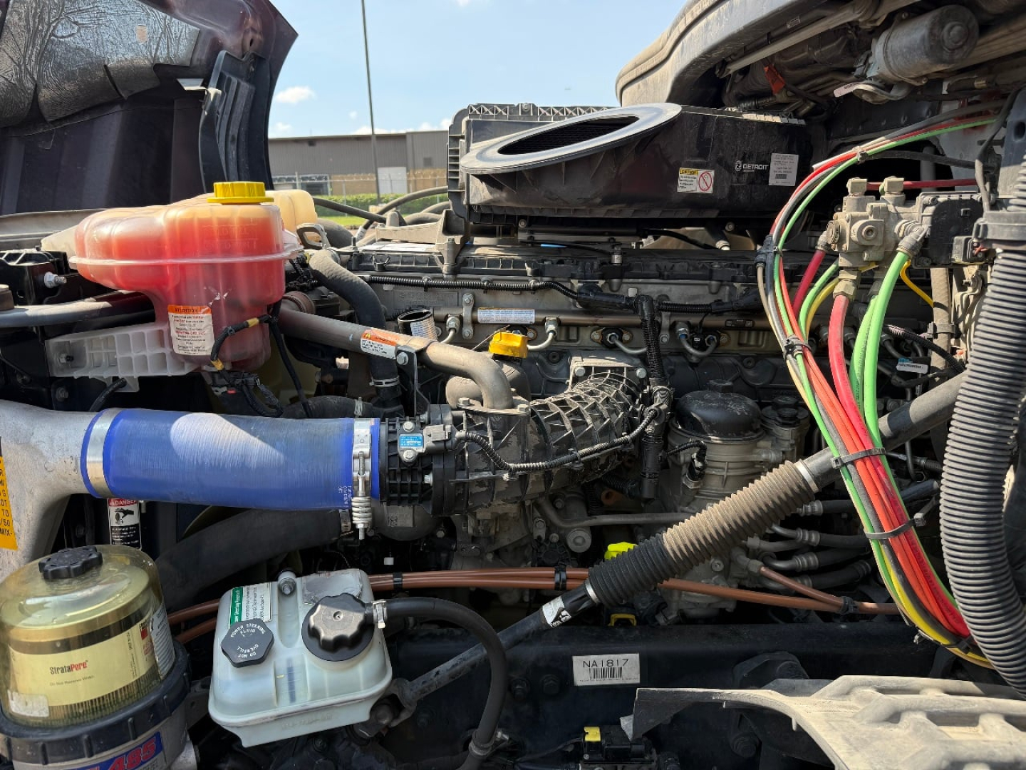 Freightliner Cascadia engine bay showing coolant reservoir, blue silicone intercooler hose, wiring harness, and various fluid reservoirs.
