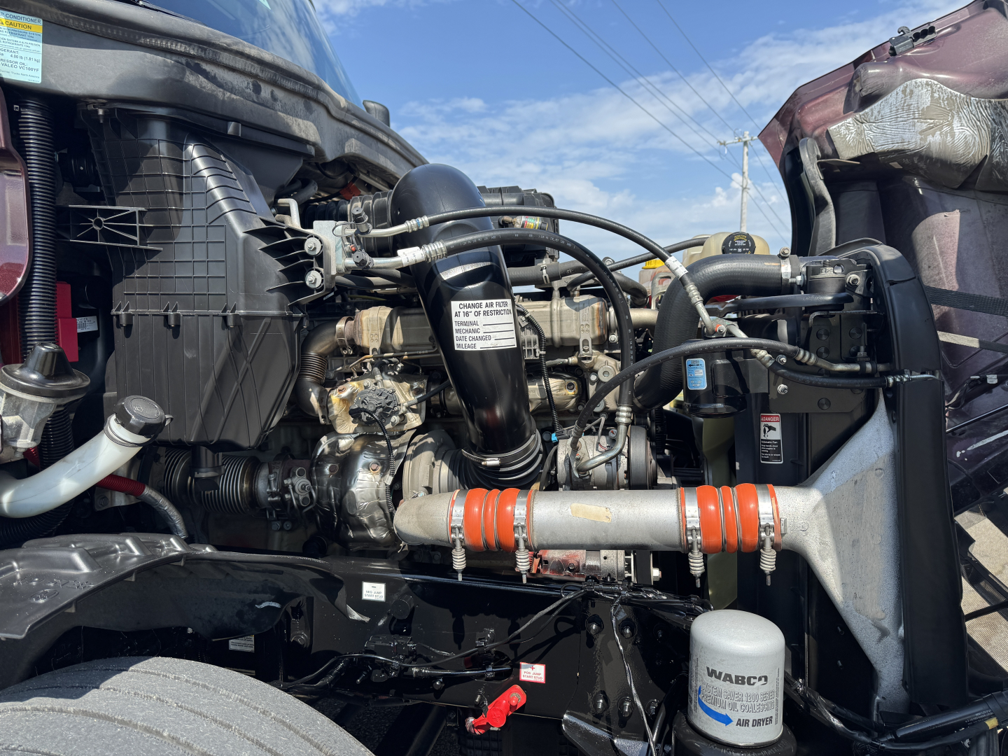 Engine bay of 2022 Freightliner Cascadia 126 showing turbocharger, hoses, intercooler, and coolant reservoir with wiring harnesses.