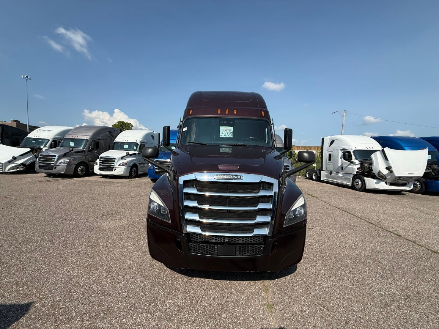 Front view of a dark maroon 2022 Freightliner Cascadia 126 semi-truck in a dealership lot with other trucks in background.