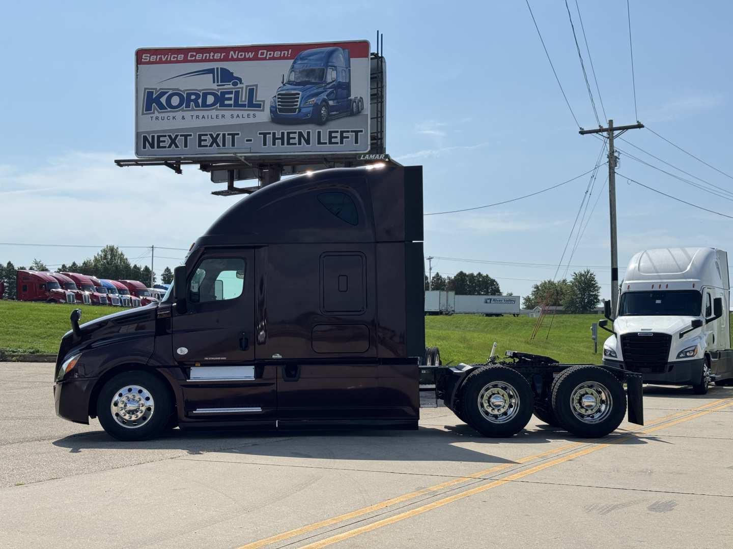 Freightliner Cascadia 126 tractor-trailer in service bay with banner sign in background; side view shows cab, sleeper, and rear axles.