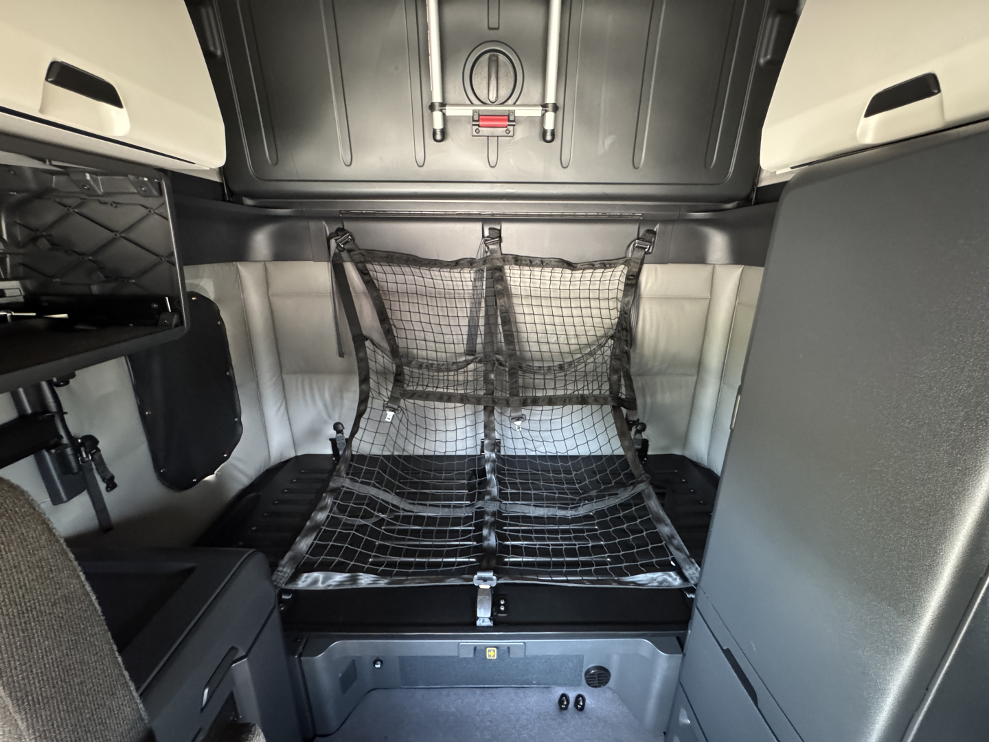 Freightliner Cascadia 126 sleeper cab interior showing bed with cargo net and surrounding storage compartments.