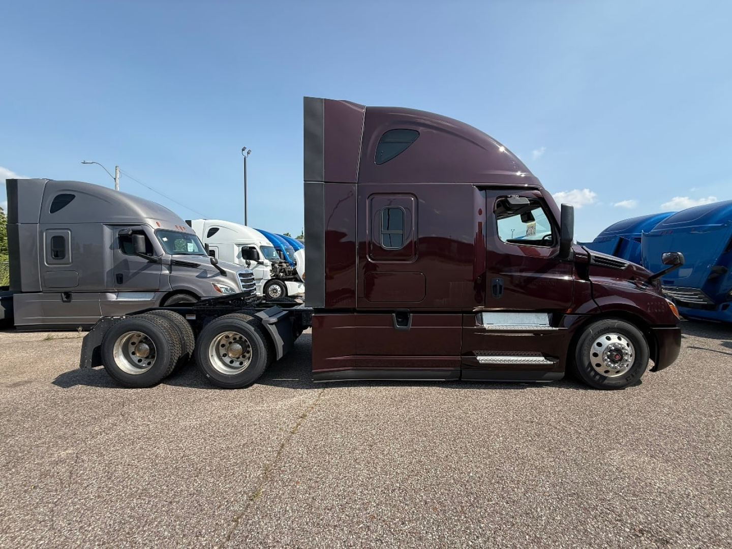 Freightliner Cascadia 126 sleeper cab tractor in profile view with maroon paint and chrome steps.