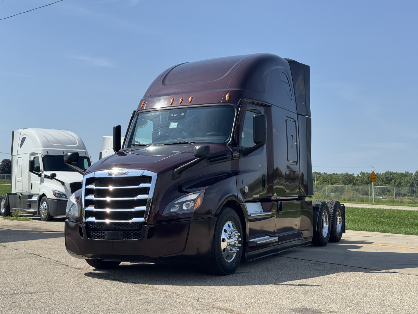Freightliner Cascadia 126 tractor-trailer in dark maroon, front three-quarter view, aerodynamic sleeper cab, chrome grille, dual rear axles, on lot.
