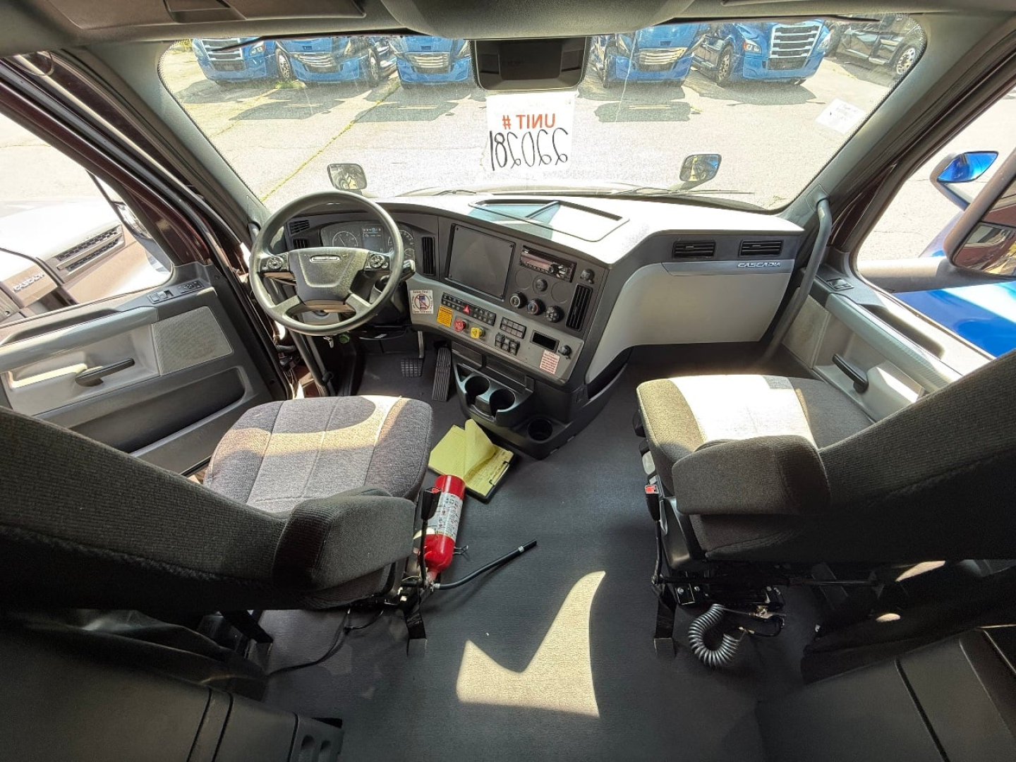 Cab interior of a Freightliner Cascadia with steering wheel, dashboard, and front seats; view from doorway, with controls and vents visible.