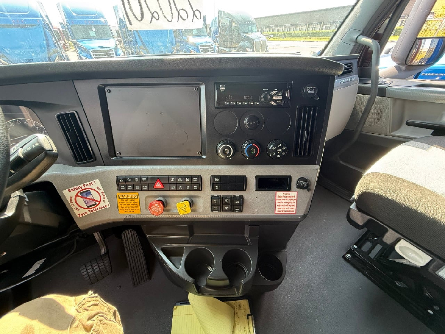 Freightliner Cascadia dash view showing touchscreen display, climate controls, and cup holders in center console.