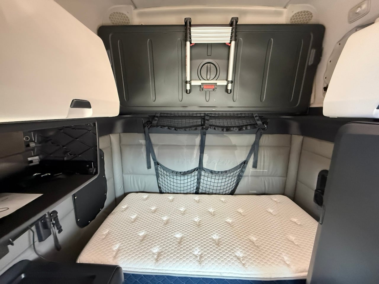 Truck cab interior storage area with mattress and overhead cabinet in a Freightliner Cascadia sleeper.