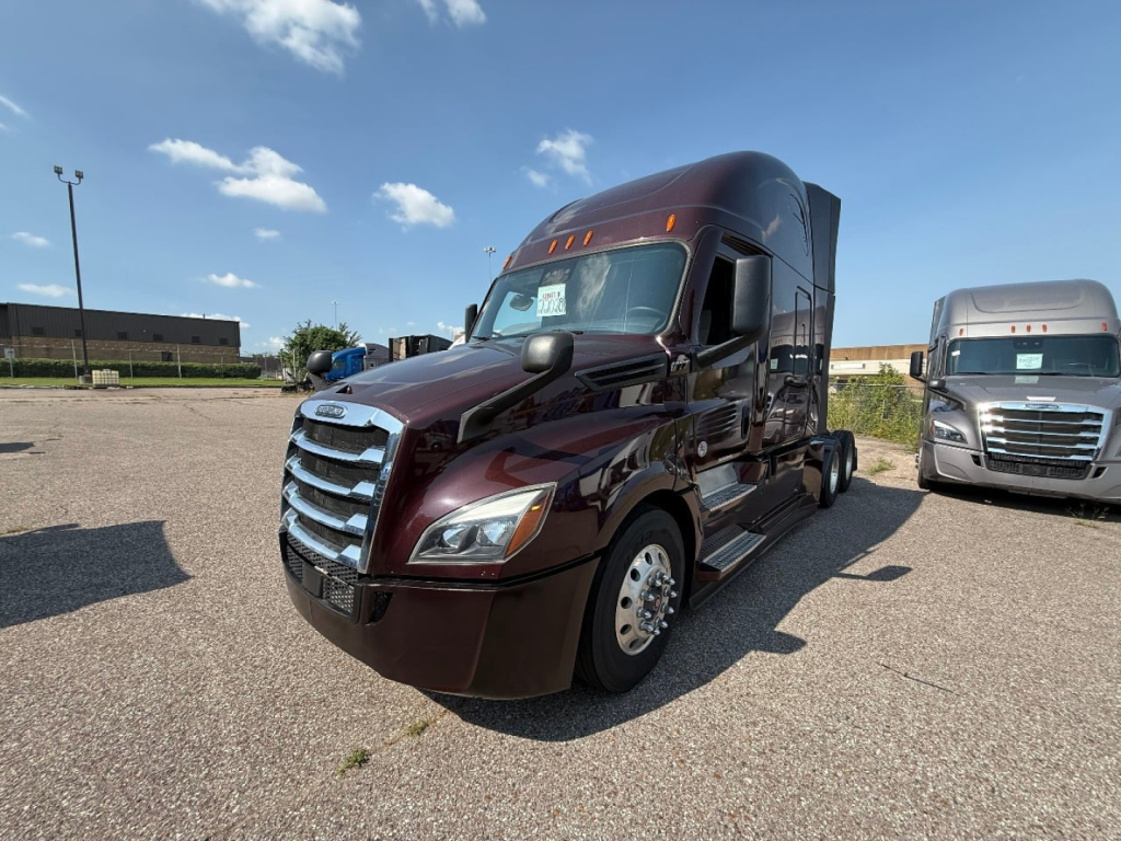 Conventional sleeper truck in a parking lot showing a maroon 2022 Freightliner Cascadia 126 tractor with chrome grille and side steps; adjacent light-colored truck in background.