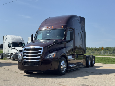 Freightliner Cascadia 126 tractor-trailer in dark maroon, front three-quarter view, aerodynamic sleeper cab, chrome grille, dual rear axles, on lot.
