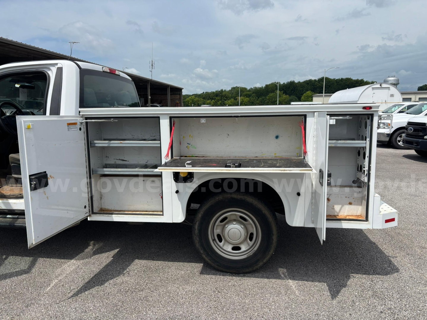 Utility bed on a Ford F-250 service truck with side cabinets open, showing compartments and storage shelves.