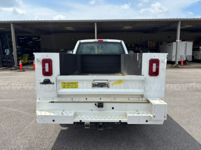 Ford F-250 rear view showing utility bed with tailgate, taillights, rear bumper, and bumper hitch. License plate reads KNAF??IDE, with yellow warning sticker on left side of tailgate.