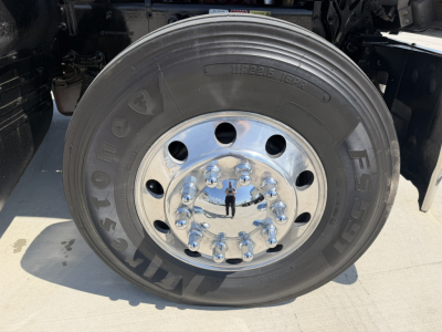 Wheel with Goodyear F Series tire and shiny chrome hub, showing lug nuts and reflection of photographer; no other text clearly visible.