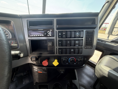 Dashboard view of a 2020 Mack PI64T truck showing radio, control switches, climate dials, and yellow and red knobs, with steering wheel partial left and passenger seat right.