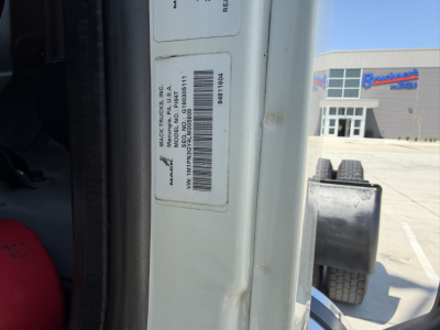 Truck door jamb showing manufacturer label with VIN barcode and stock number at a Mack truck yard.