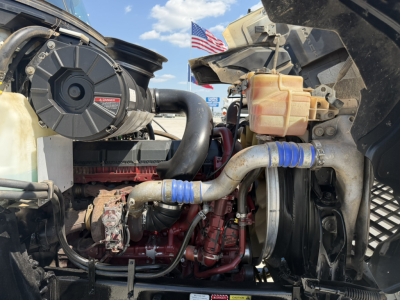 Mack PI64T engine bay showing intake components, radiator hoses, suspensions, and engine block with red paint; visible hoses with blue clamps and a coolant reservoir.