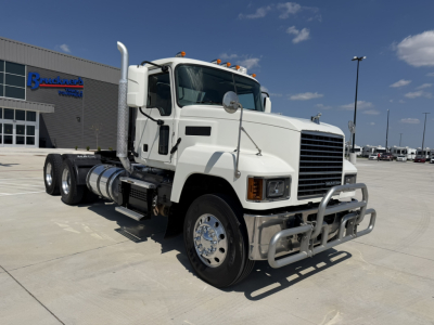 Truck: 2020 Mack PI64T conventional daycab, white, front bull bar, dual rear axles, large chrome wheels, exhaust stack, side fuel tanks, upfront view showing grille and headlights.