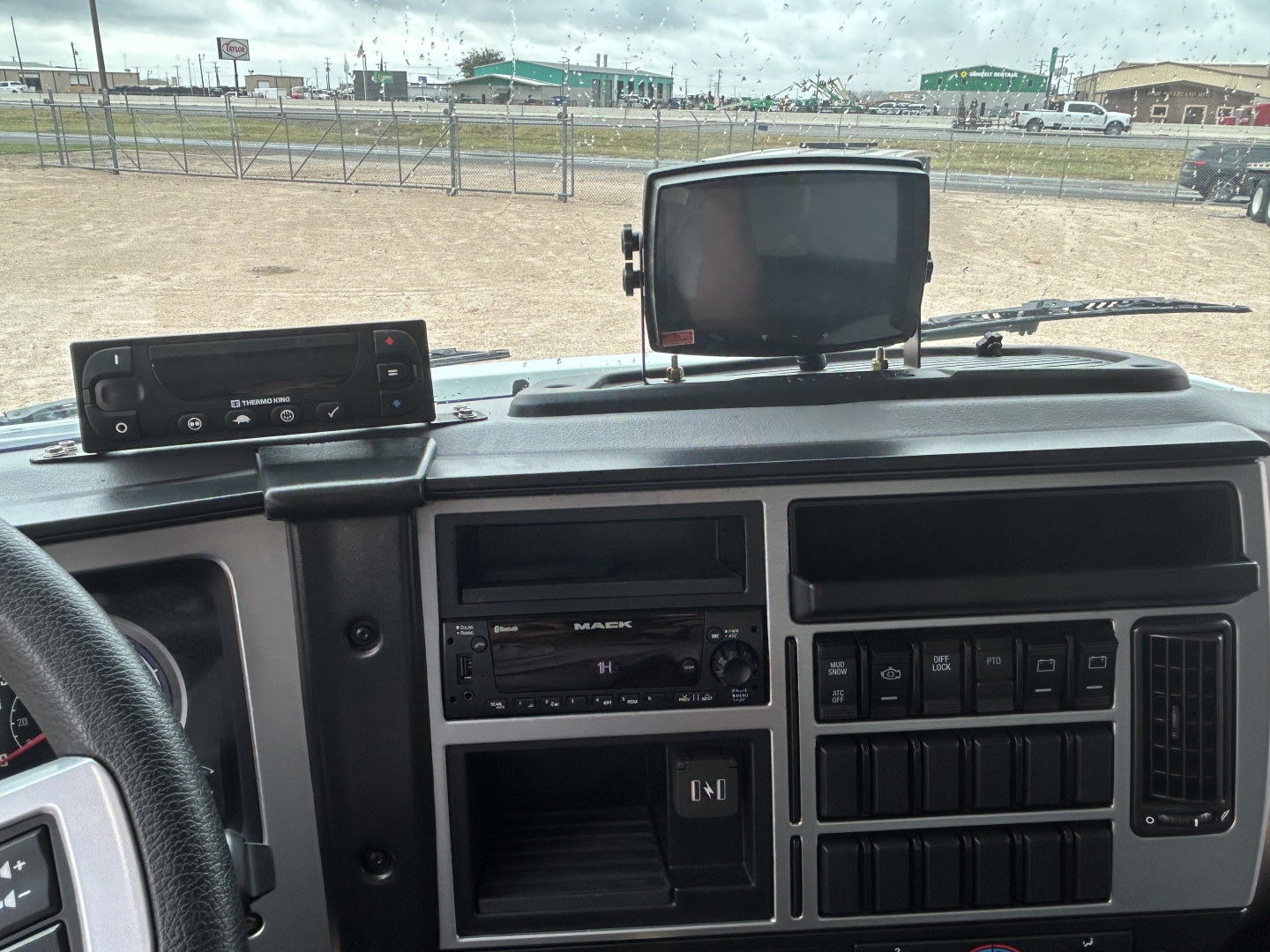Truck cab interior of 2026 Mack MD6 showing instrument panel, radio, switches, and a dash-mounted GPS/monitor unit.