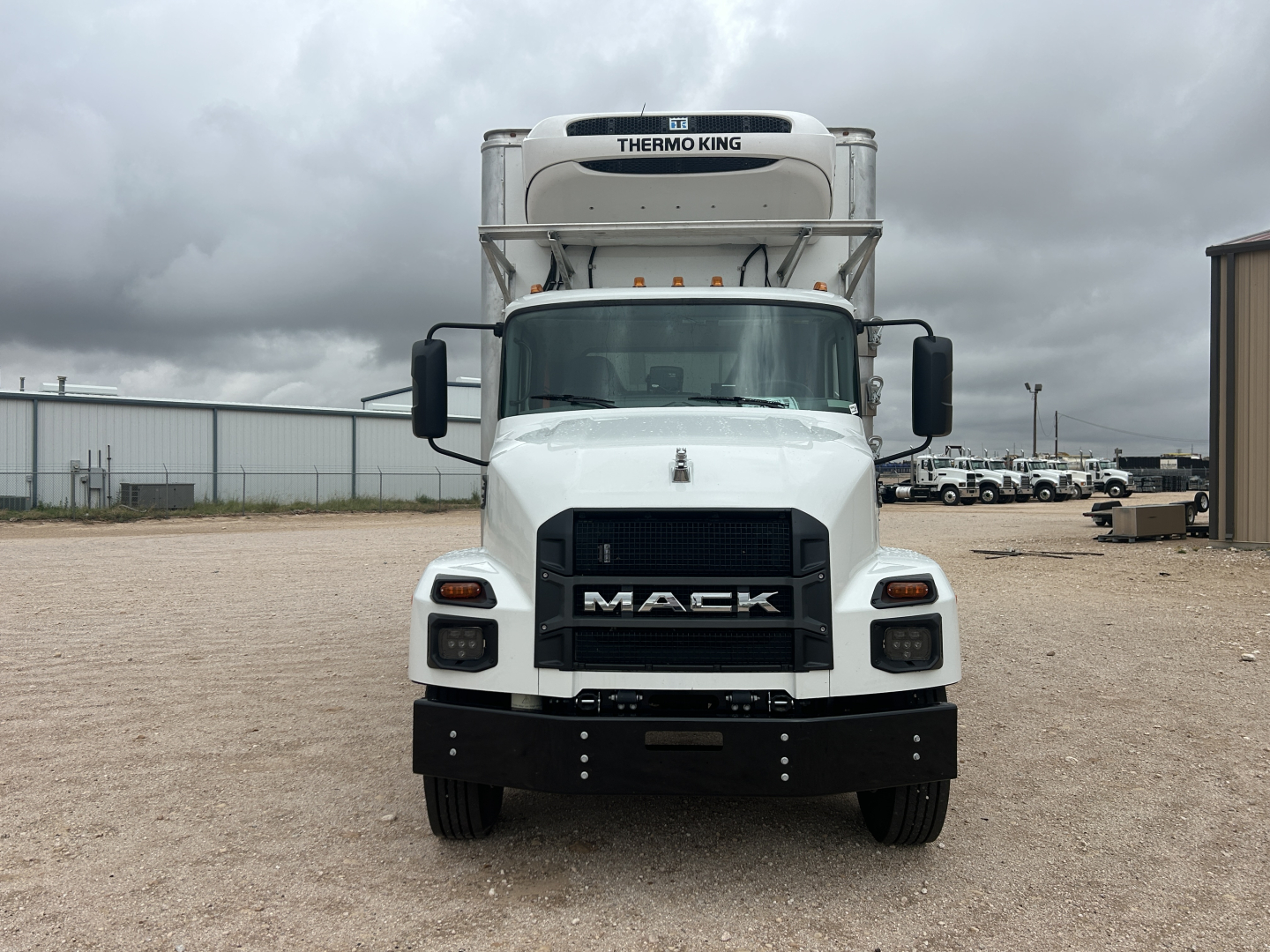 Front view of a white 2026 Mack MD6 refrigerated truck with Thermo King unit on top, large black Mack grille, black bumper, side mirrors, and cargo area visible in background.